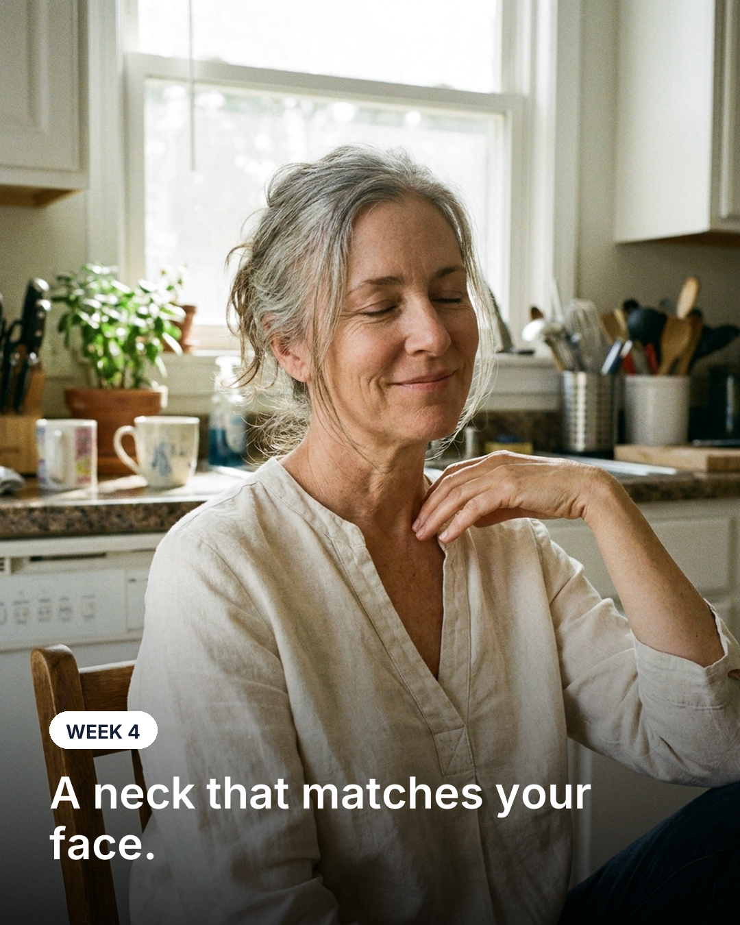 A woman in her kitchen with one hand resting at her neck